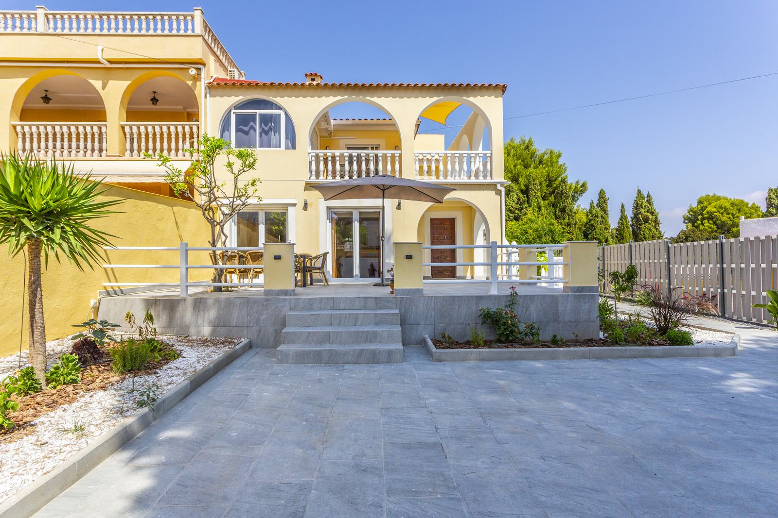 Villa Sonrisa: gelbe Villa mit Rundbögen, Terrasse und Palme unter blauem Himmel